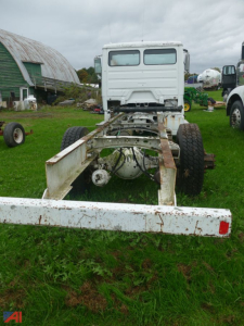 Rear view of a Freightliner FL70 chassis cab showing bare frame, drivetrain area, and dual rear wheels, with white cab at the front and overcast sky.