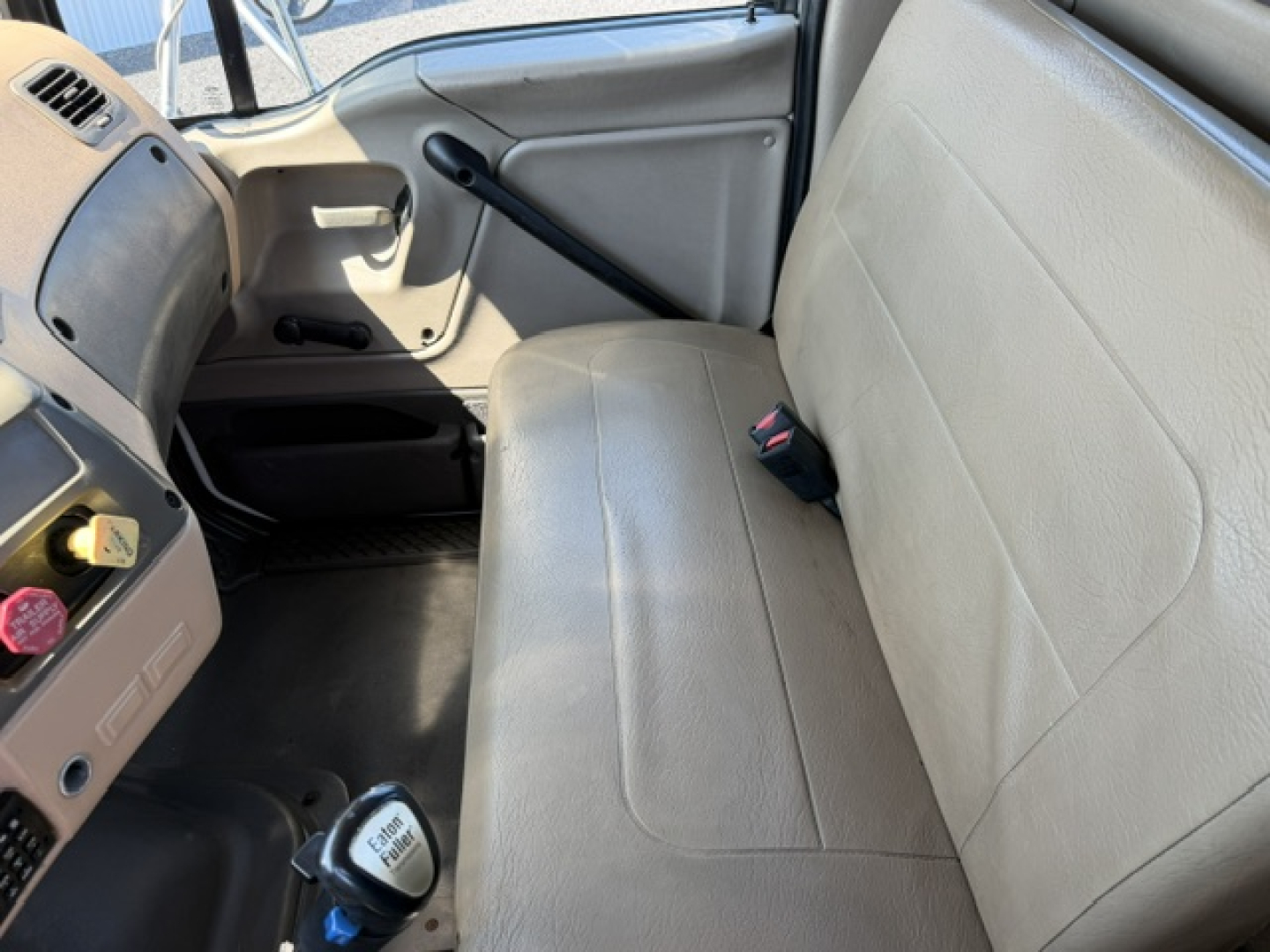Vehicle cab interior of a 2006 Sterling LT9500 truck with a light gray bench seat, manual window crank, and steering column area visible.