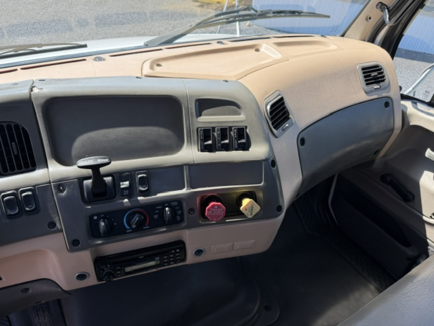Dashboard of 2006 Sterling LT9500 cab showing steering wheel on left, climate controls, radio slot, and glove compartment; central console with round blue knob and red/pink caps.