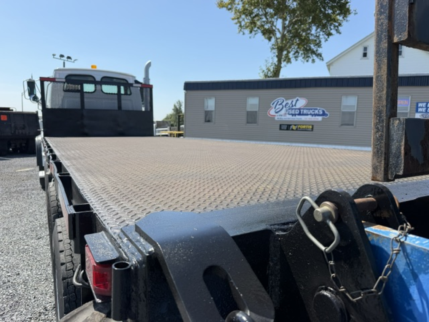 Flatbed truck bed of a 2006 Sterling LT9500 with diamond plate steel deck, rear taillights, and wheel chocks; Best Used Trucks sign in background.