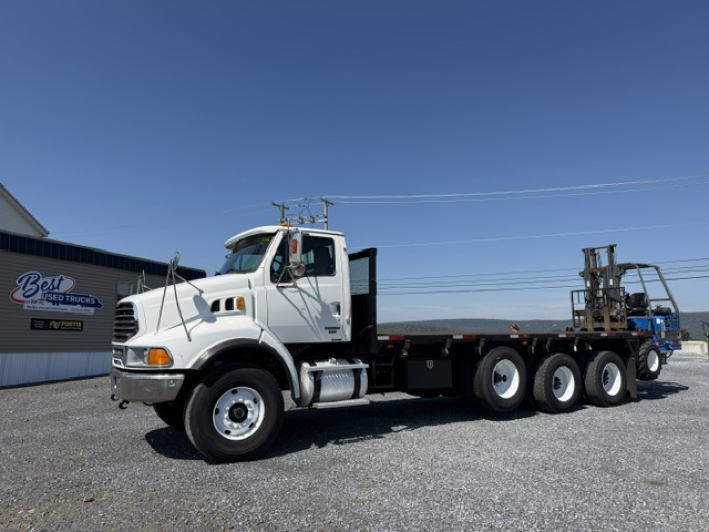 2006 Sterling LT9500 flatbed truck with multiple axles and a crane accessory in the bed, side view showing cab and flatbed.