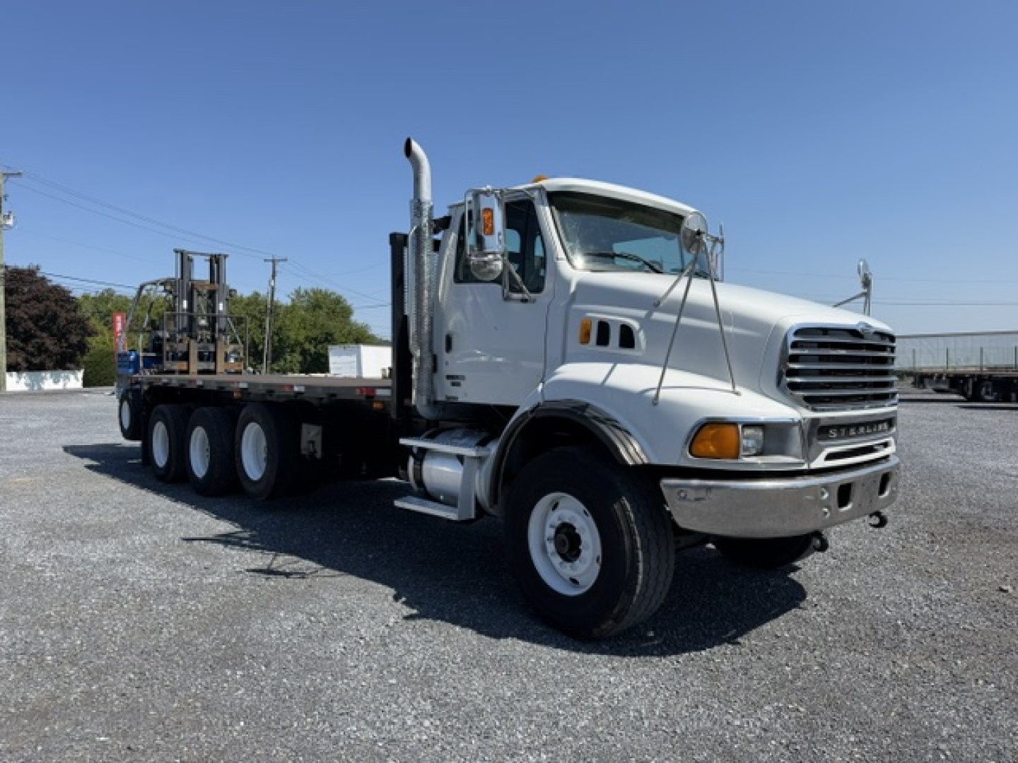 Flatbed truck showing Sterling LT9500 cab and long heavy-duty trailer with multiple axles in a gravel lot.