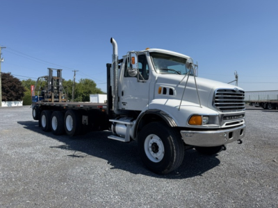 Flatbed truck showing Sterling LT9500 cab and long heavy-duty trailer with multiple axles in a gravel lot.