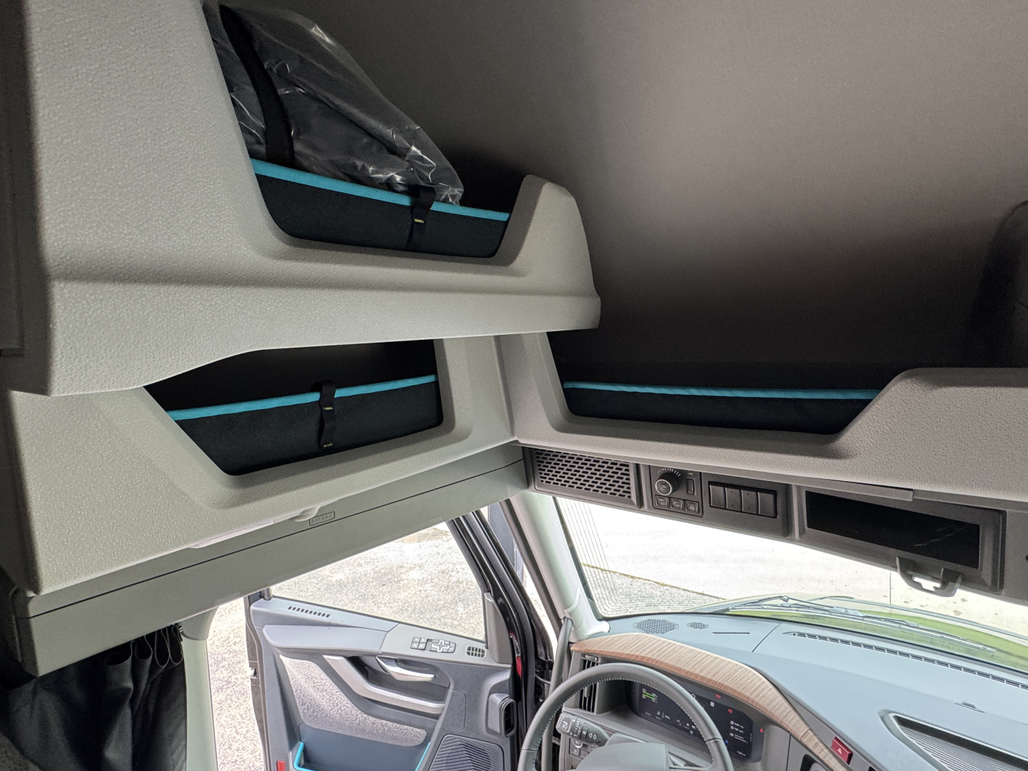 Cab interior of a Volvo VNL truck showing overhead storage compartments and dash area; light gray panels with blue accents.