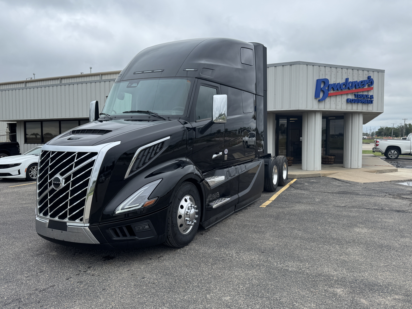 Volvo VNL64T860 conventional sleeper truck in black, front and side view, showing chrome grille, large cab, and sleeper behind cab.