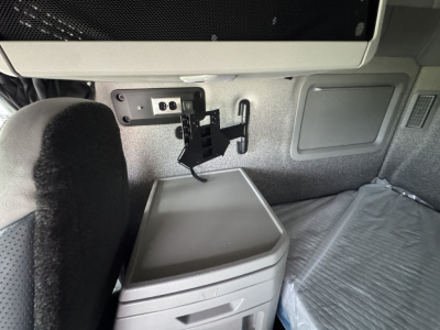 Truck cab interior showing dashboard panel and mounted device with power outlet and storage bin in a Volvo VNL64T860 sleeper.