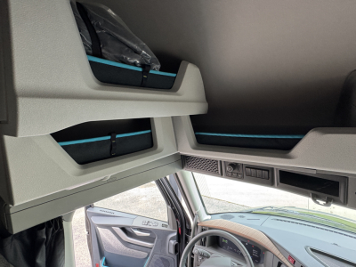 Cab interior of a Volvo VNL truck showing overhead storage compartments and dash area; light gray panels with blue accents.