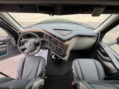 Volvo VNL64T860 truck interior showing steering wheel and dashboard with dual seats and center console; instrument cluster and sun visors visible.