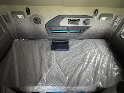 Volvo VNL64T860 sleeper cab interior showing bed area with plastic cover, overhead control panel, two circular speakers, and storage compartments.
