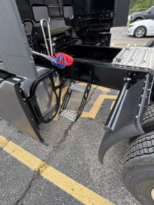  Volvo VNL64T860 tractor-trailer cab area showing steps and access ladder, air lines, and wiring near the fifth wheel mounting.