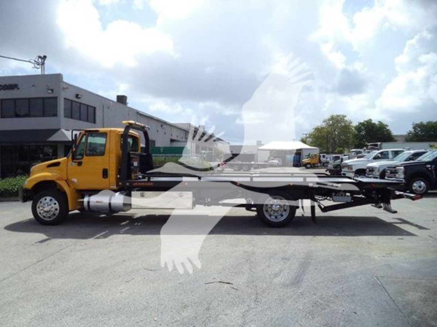 Truck mounted tow bed with yellow cab and long flatbed, side view showing rollback equipment and chassis.