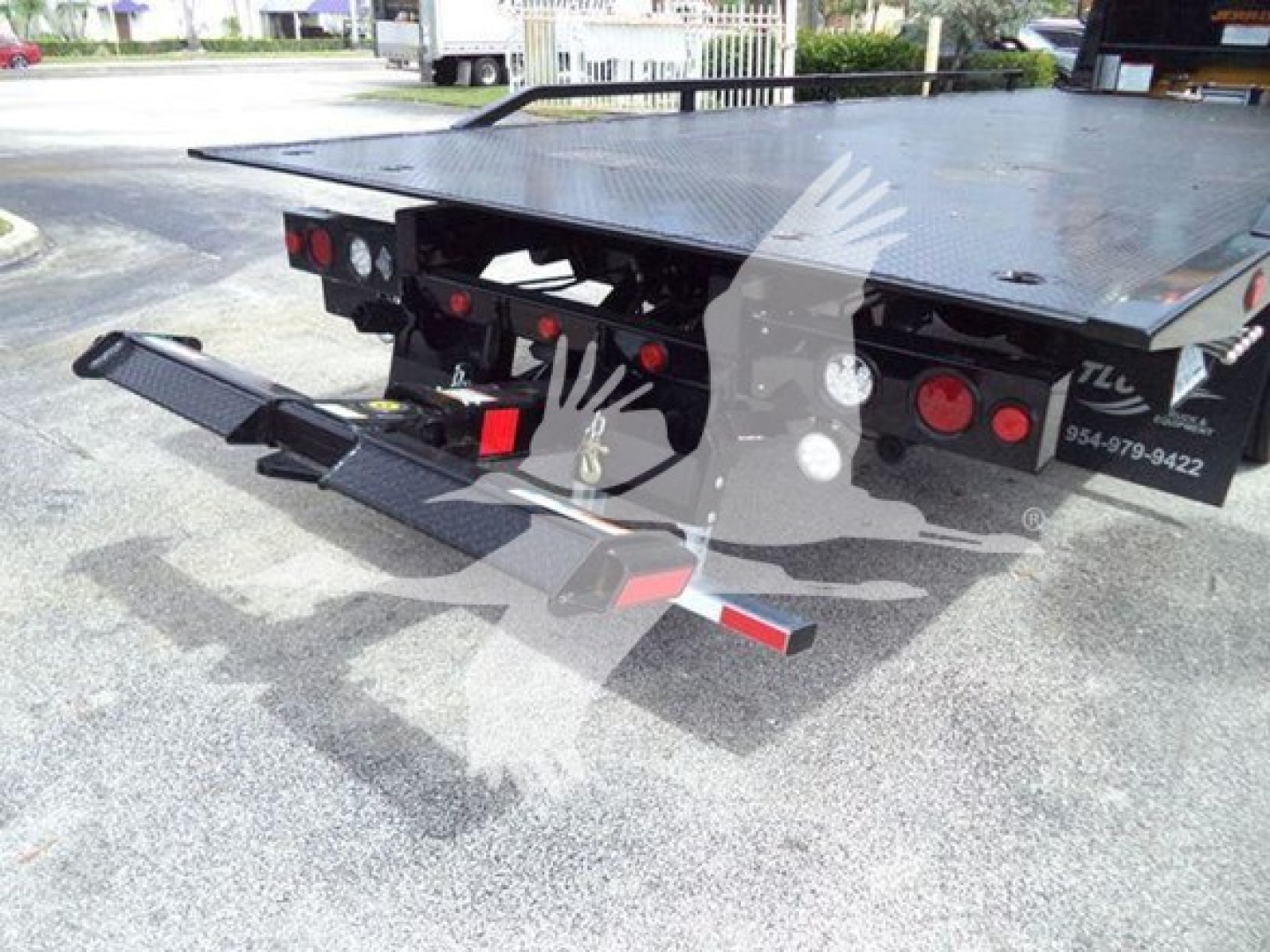 Tow truck platform rear with hydraulic rollback bed and twin rear bumper arms, rear lights visible.