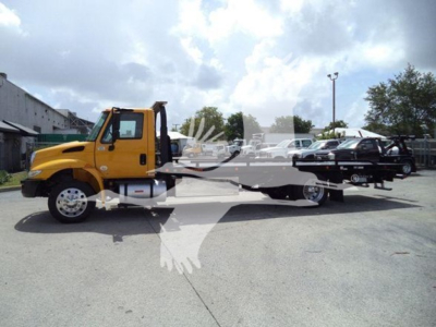 Tow truck/rollback with yellow cab and flatbed, International Durastar model, visible text on vehicle and surrounding lot.
