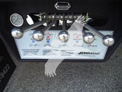 Control panel with five silver toggle knobs and a gauge on left, instructional label with JERB-DAN branding, part of a rollback truck undercarriage.