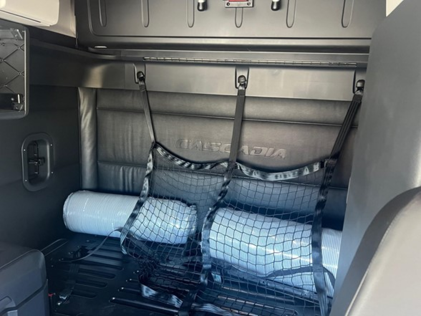 Truck interior showing storage area behind cab with a roll-up mat and a mesh cargo bag, Freightliner Cascadia 126 branding on side panel.