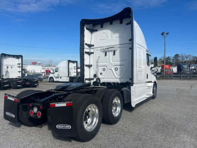 Side rear view of a white Freightliner Cascadia 126 tractor in a lot, showing the sleeper cab and dual rear axles.