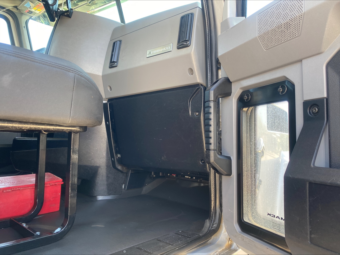 Truck cab interior showing dashboard side panel and door frame with storage area and a black panel; view from passenger side floor area.