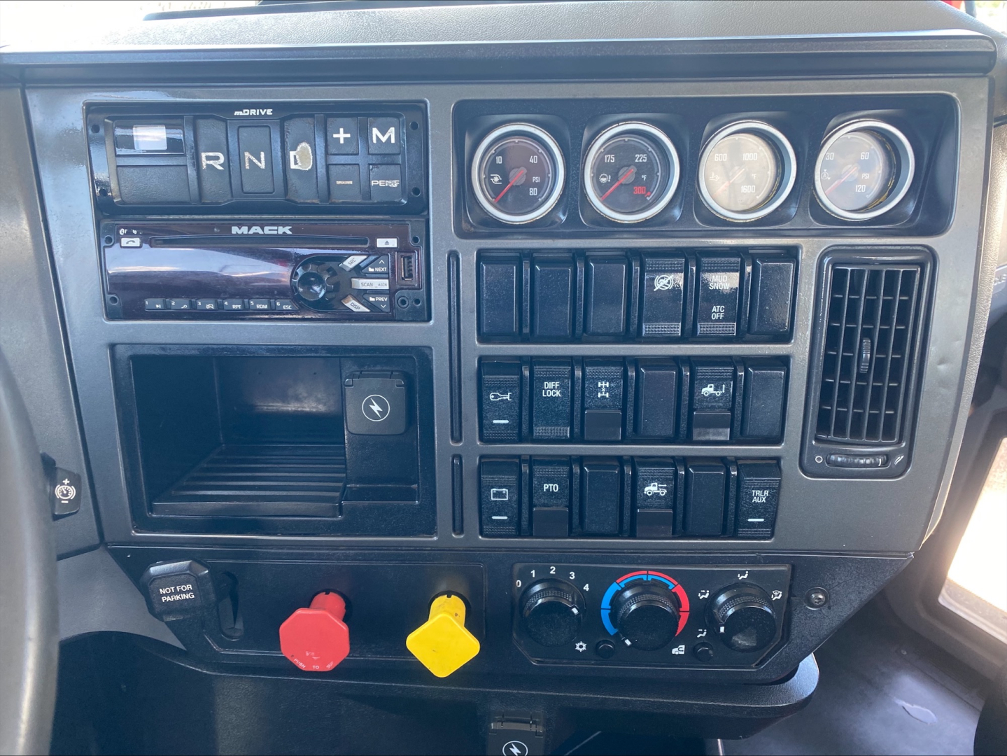 Dashboard of 2019 Mack PI64T conventionals daycab showing gear selector with R N D M, gauges, switches, and climate controls; red and yellow knobs; MP battery or power panel visible.
