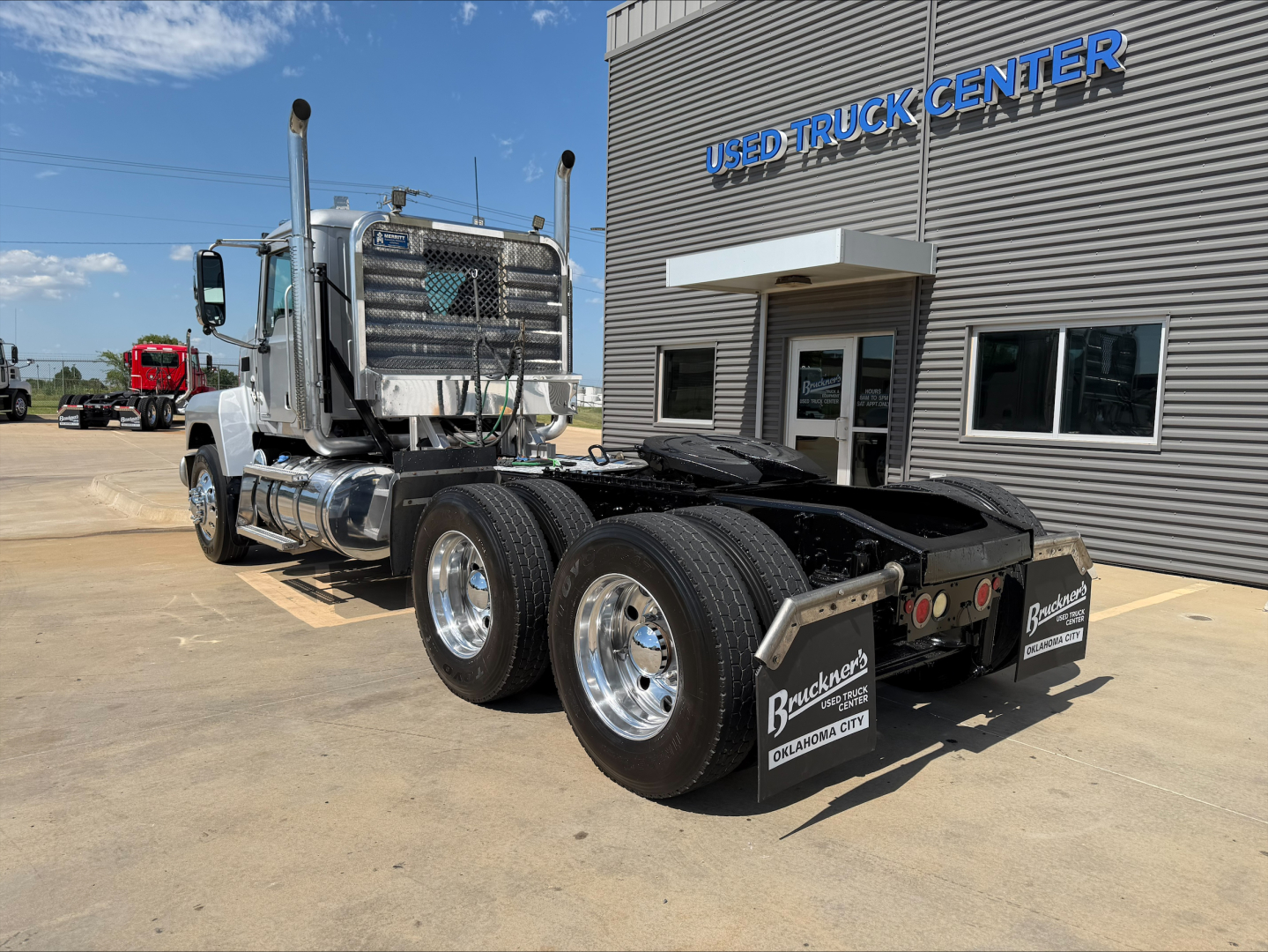 Mack PI64T daycab tractor shown from rear-left angle with dual rear axles and chrome wheels, parked outside a used truck center.