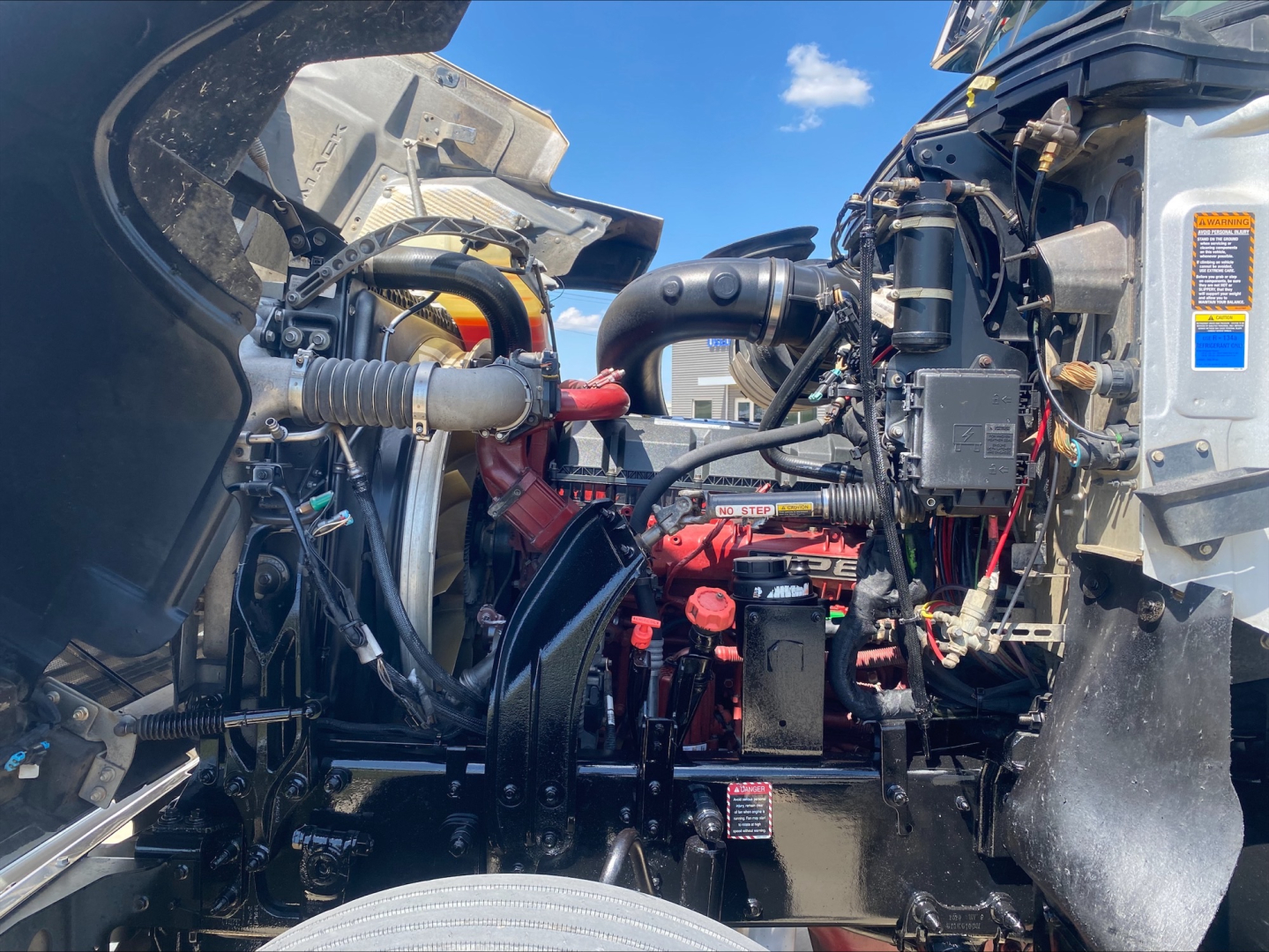 Truck engine bay view of a 2019 Mack PI64T showing engine components, hoses, and wiring with red engine block and black frame