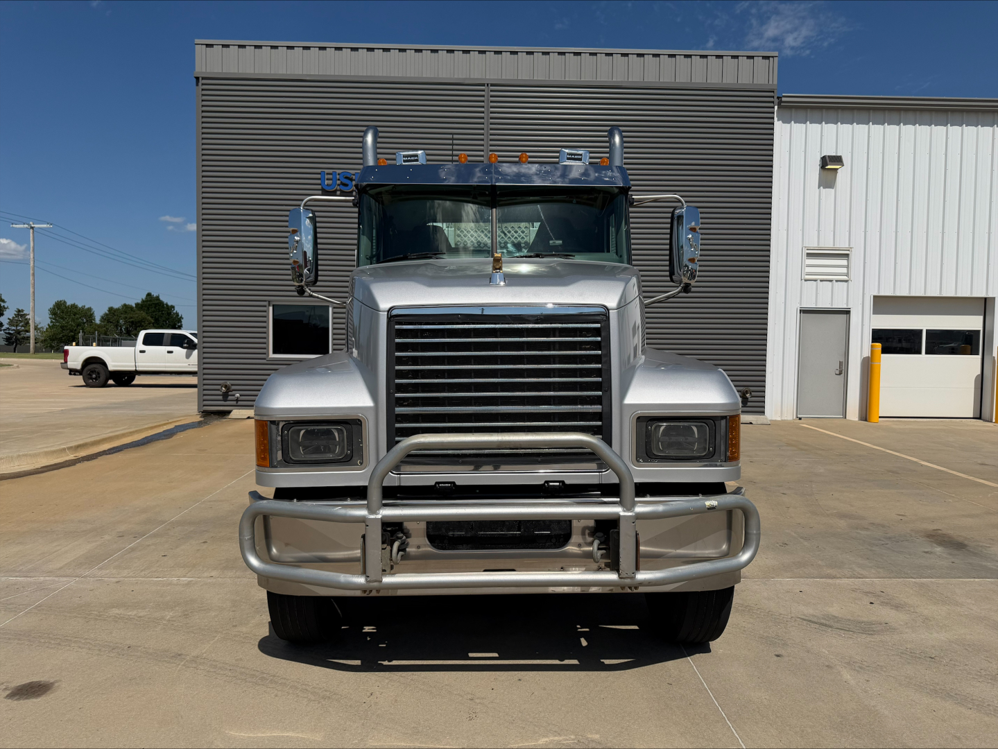 Mack PI64T conventional daycab truck front view showing chrome grille, bumper guard, large headlights, and mirrors.