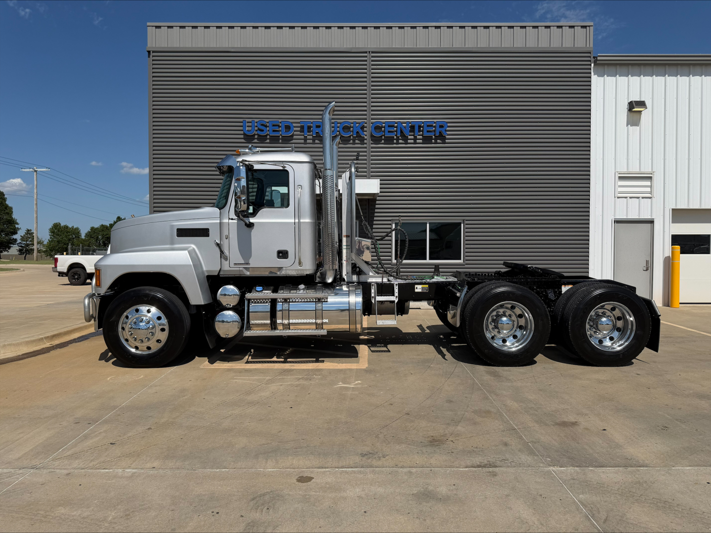 2019 Mack PI64T conventional daycab truck viewed in profile at a dealership lot with a gray cab and chassis, Used Truck Center building in background.