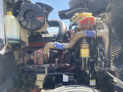 Engine bay of a 2019 Mack PI64T conventional daycab showing coolant reservoir, turbocharger, hoses, and fluid reservoirs.