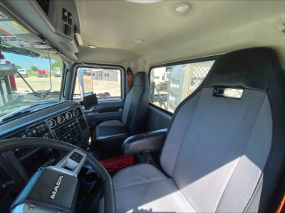 Cab interior of a 2019 Mack PI64T truck showing driver seat, steering wheel, dashboard with gauges, and passenger seat; windshield and side windows visible.
