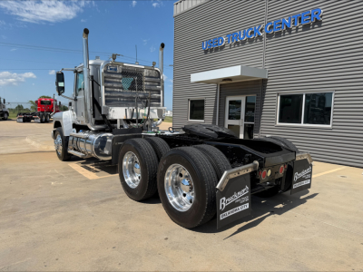 Mack PI64T daycab tractor shown from rear-left angle with dual rear axles and chrome wheels, parked outside a used truck center.