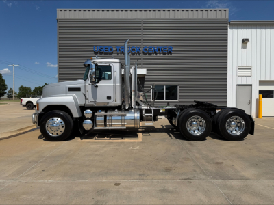 2019 Mack PI64T conventional daycab truck viewed in profile at a dealership lot with a gray cab and chassis, Used Truck Center building in background.