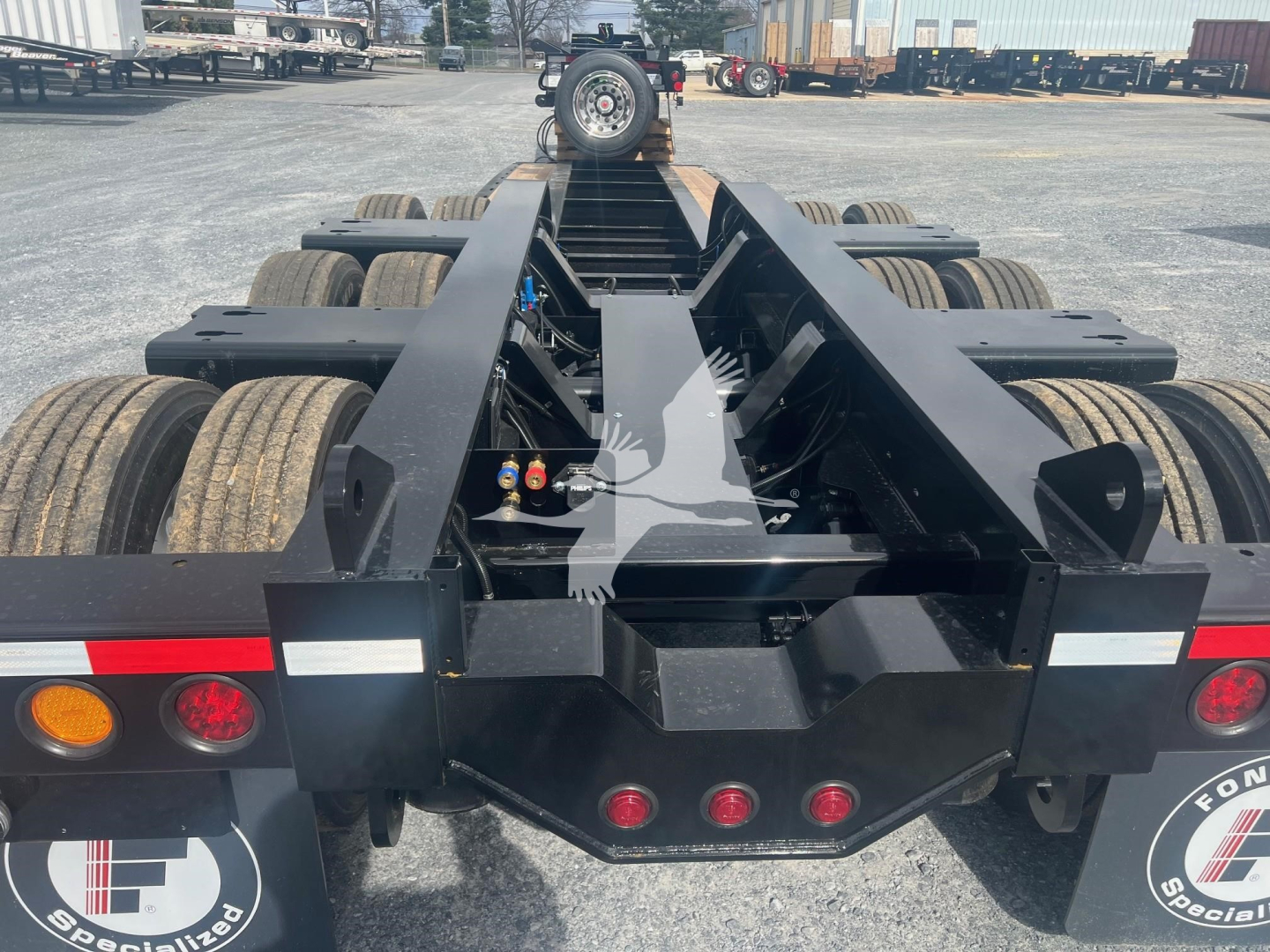 Lowboy trailer chassis frame with multiple axles and rear coupler hub, black paint, reflective lights and Fender, Fontaine Magnitude 55H-Dsr branding not visible.