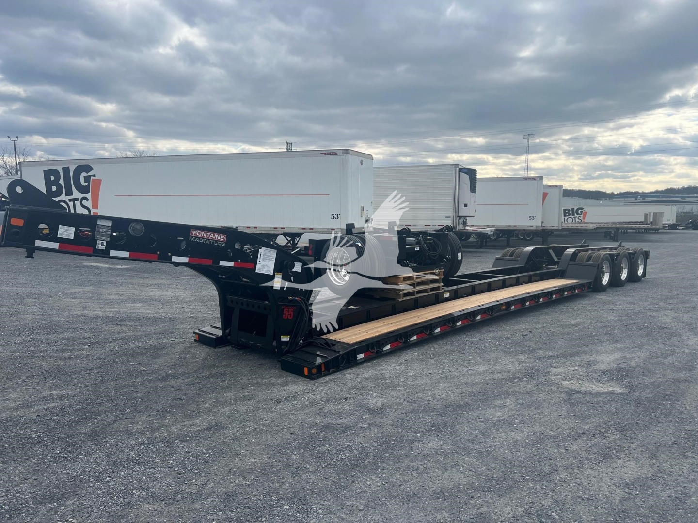 Lowboy trailer with multiple axles and a Fontaine Magnitude 55H-Dsr model, shown in an outdoor yard with other trailers in background.