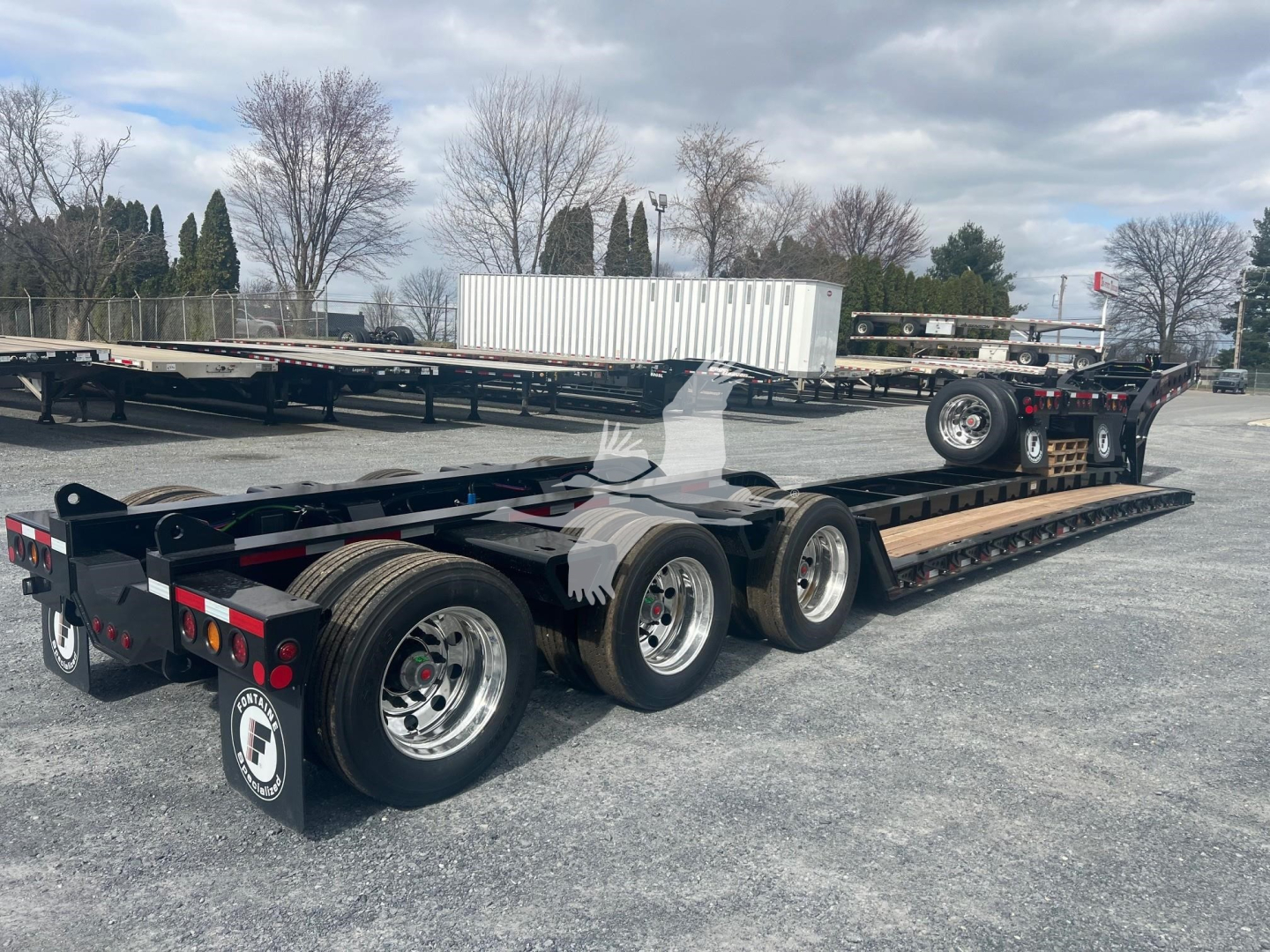 Lowboy trailer from Fontaine Magnitude 55H-Dsr series with triple axle configuration and flatbed, showing rear and side profile with spare tire and landing gear.