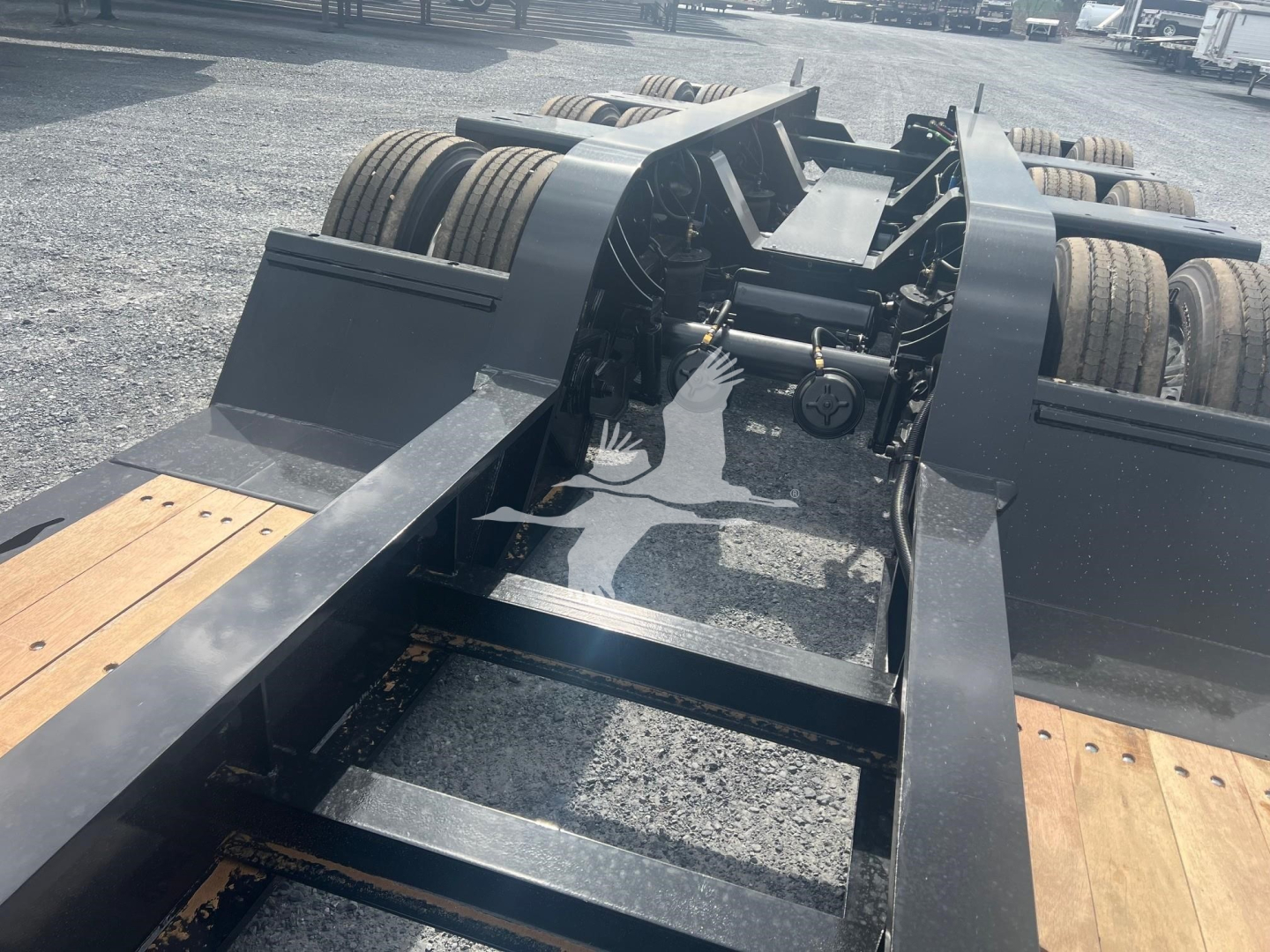 Lowboy trailer chassis with fifth wheel area and drivetrain visible; frame and steps shown.