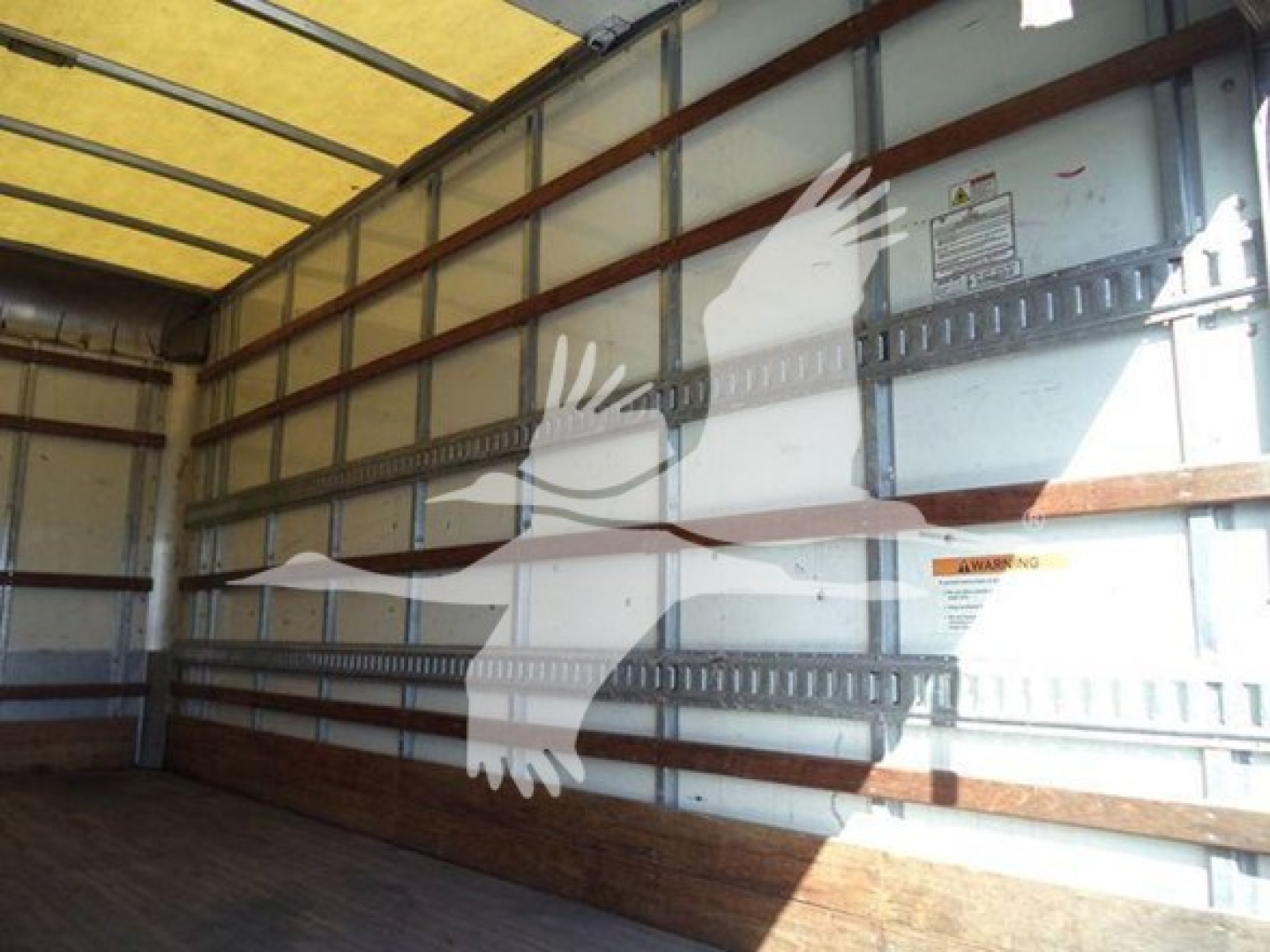 Isuzu NPR-HD box truck interior viewed from side with metal wall panels and wooden floor, no cargo.
