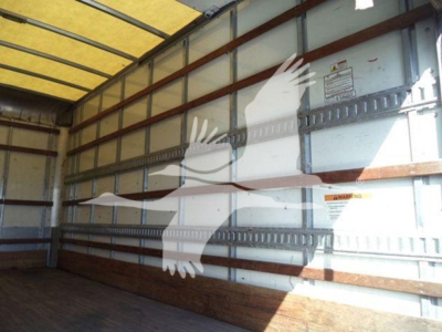 Isuzu NPR-HD box truck interior viewed from side with metal wall panels and wooden floor, no cargo.