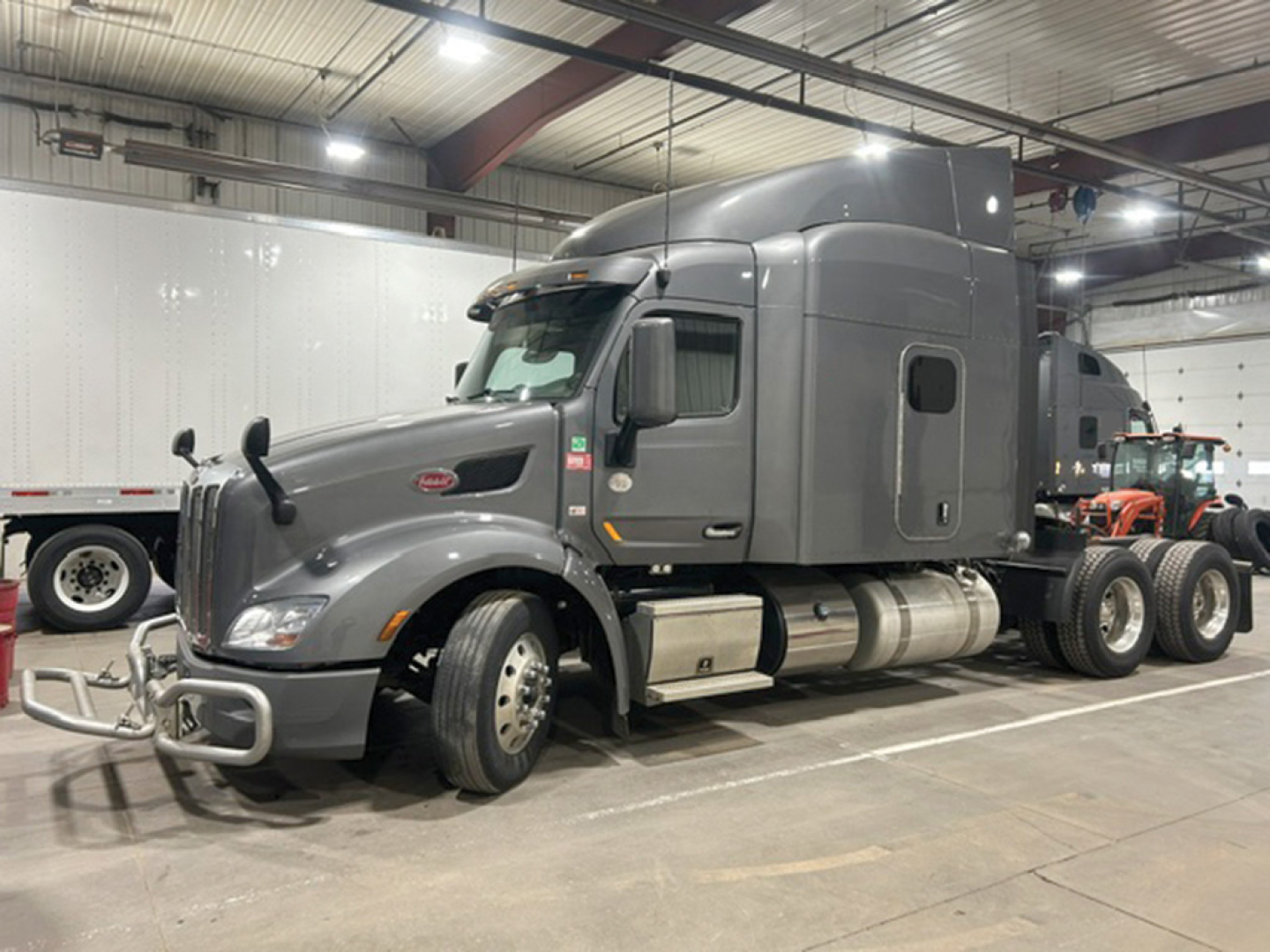 Peterbilt 579 UltraCab tractor in a showroom bay, grey exterior, single sleeper model, front and side view with chrome bumper guards.