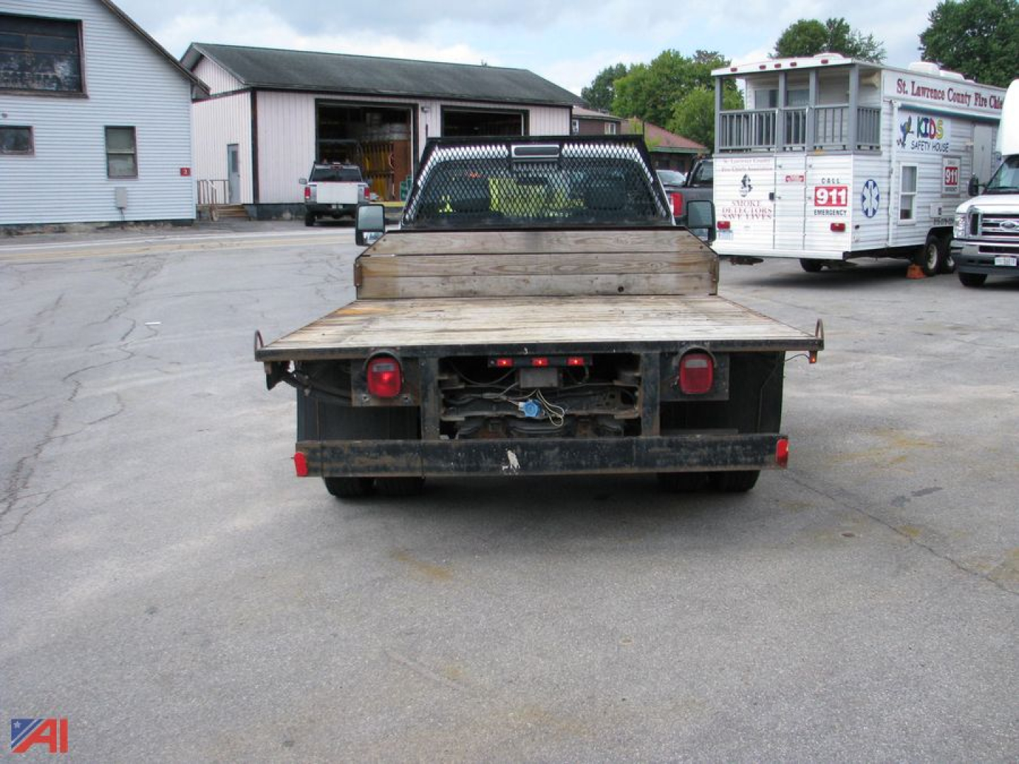 Truck flatbed rear view showing dual rear wheels and wooden bed with taillights.