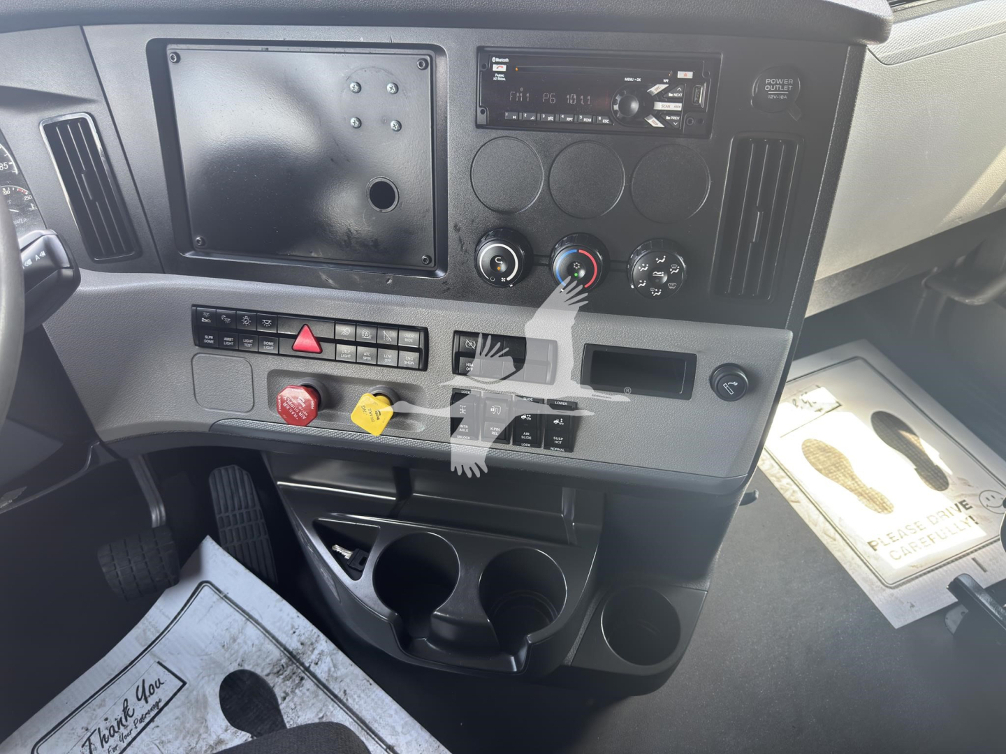 Dashboard area of a Freightliner Cascadia 126 showing climate controls, radio, and switch panel with three circular controls and cup holders.