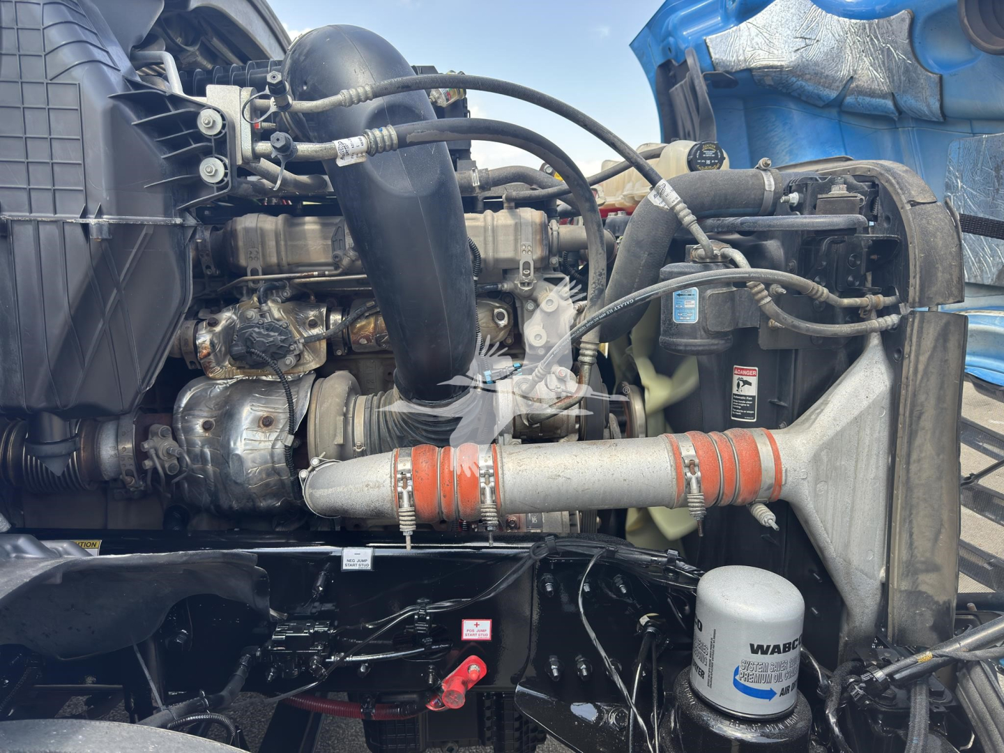 Engine bay of a Freightliner Cascadia 126 with visible hoses, turbo, intercooler, and auxiliary filters. Text on a white oil/air filter near front shows MA. Dash of engine with cables and metal pipes.