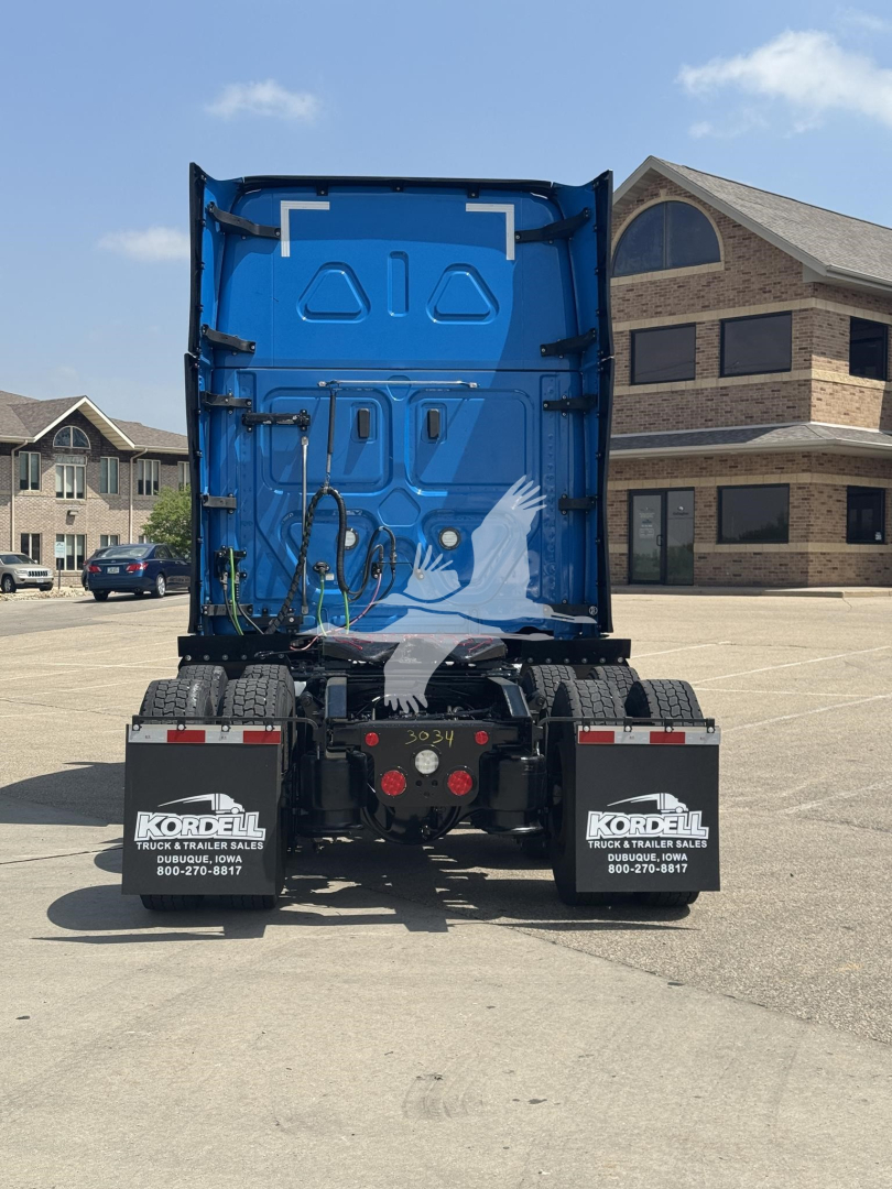 Back of a blue Freightliner Cascadia 126 truck cab in a parking lot, with rear wheels and mud flaps showing KORD dual mudflaps, and a painted design on the tailgate.