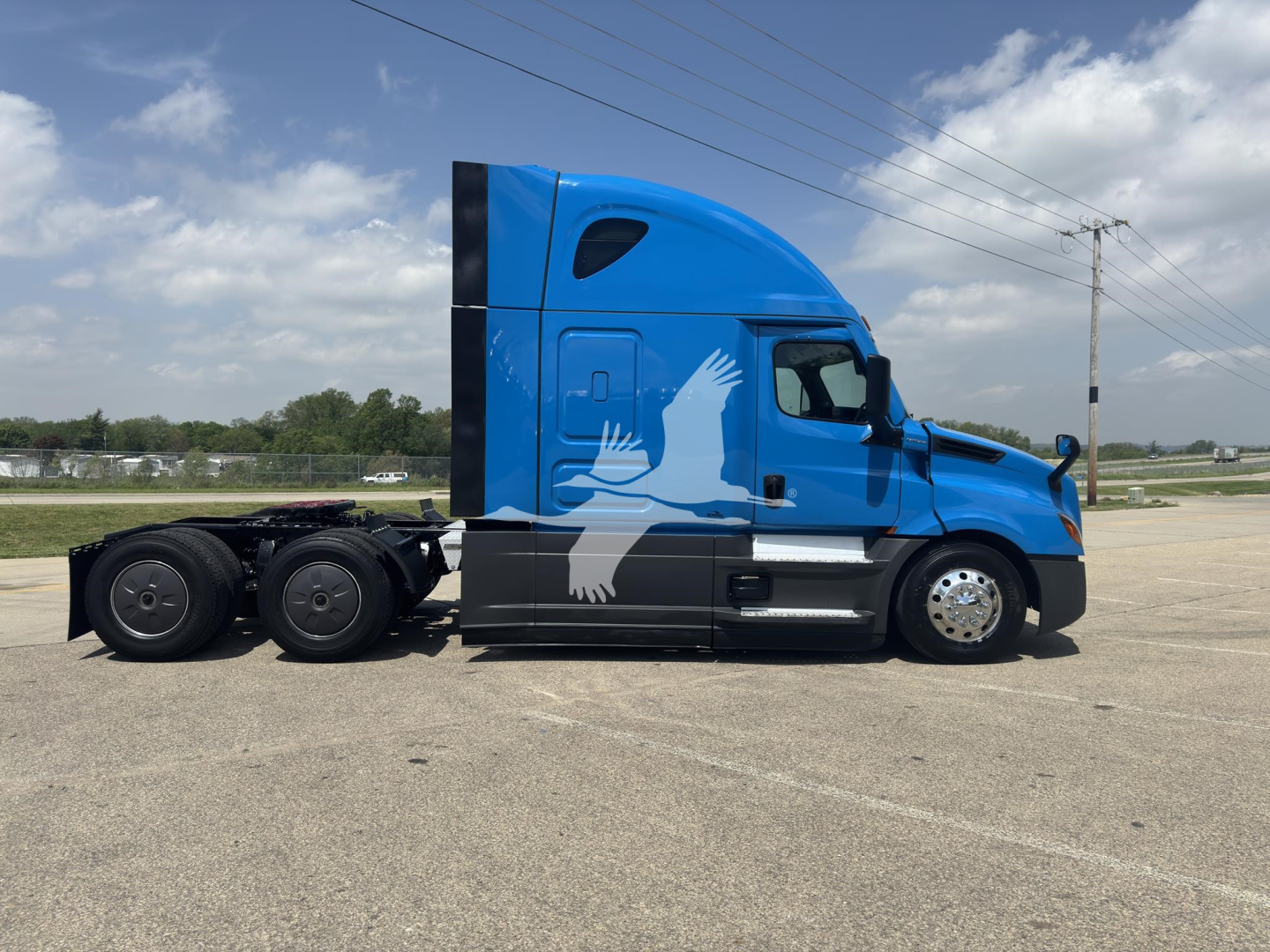 Truck side profile of a blue 2023 Freightliner Cascadia 126 conventional sleeper with a black lower body and graphic white eagle design on the cab.
