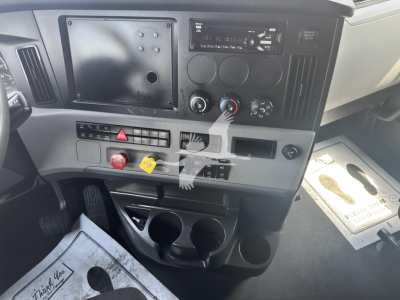 Dashboard area of a Freightliner Cascadia 126 showing climate controls, radio, and switch panel with three circular controls and cup holders.