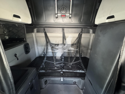Freightliner Cascadia 126 sleeper cab interior showing cargo area with netting and bed, side storage panels, and overhead ceiling.