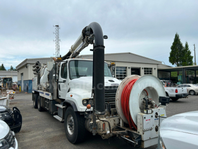 Truck body with a long vacuum hose reel and mounted hose reel on a white Freightliner unit in a yard.