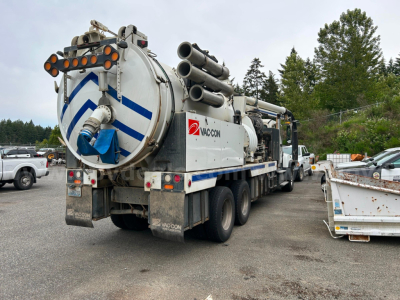 Rear of a Freightliner vacuum truck with cylindrical vacuum tank, hoses, and Vacon branding showing circular rear lights and dual rear tires.