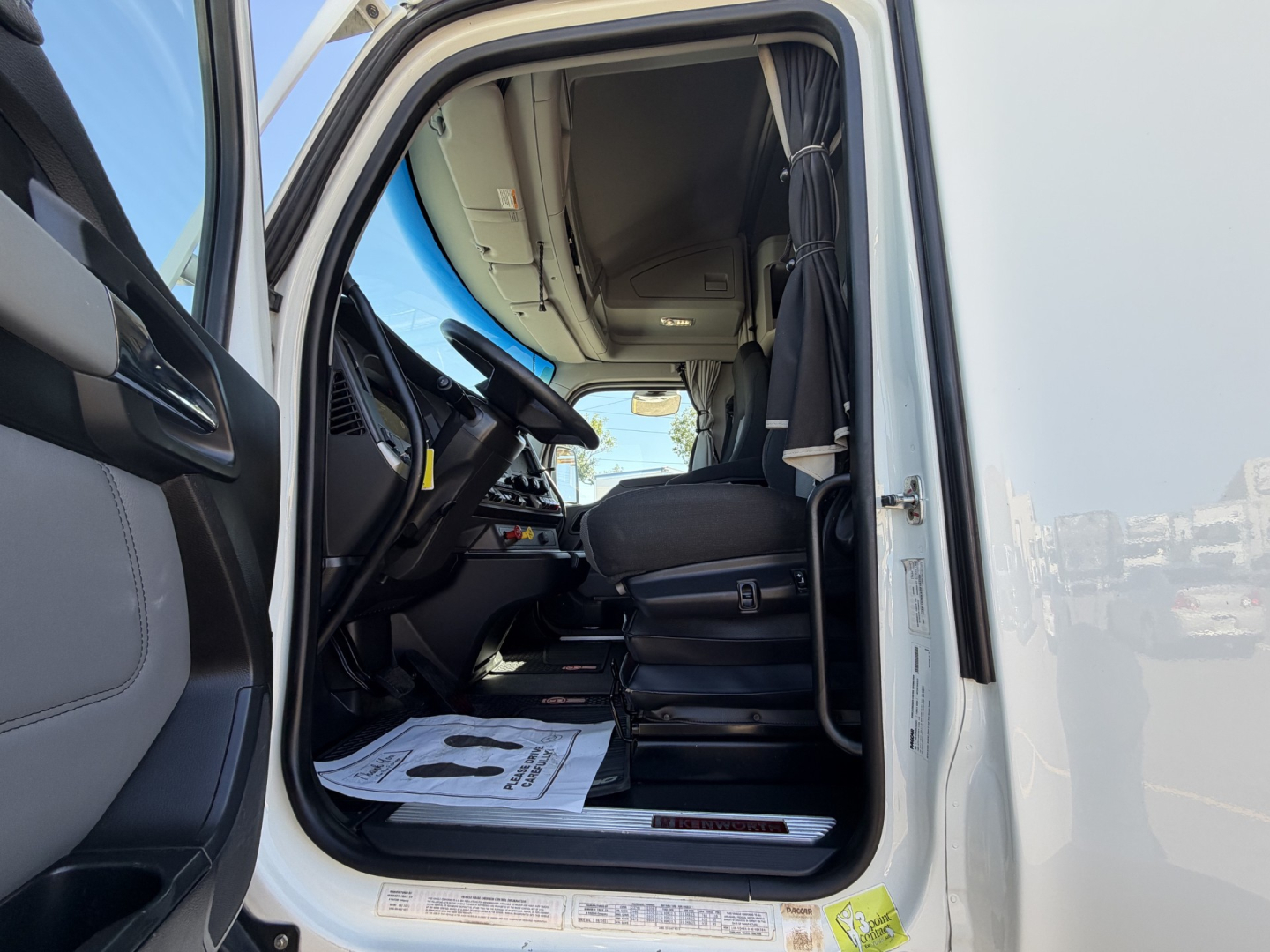 Truck cab interior view of a 2022 Kenworth T680 with driver seat visible, steering wheel, dashboard, and open door; VMIN and stock details not visible in text on image.
