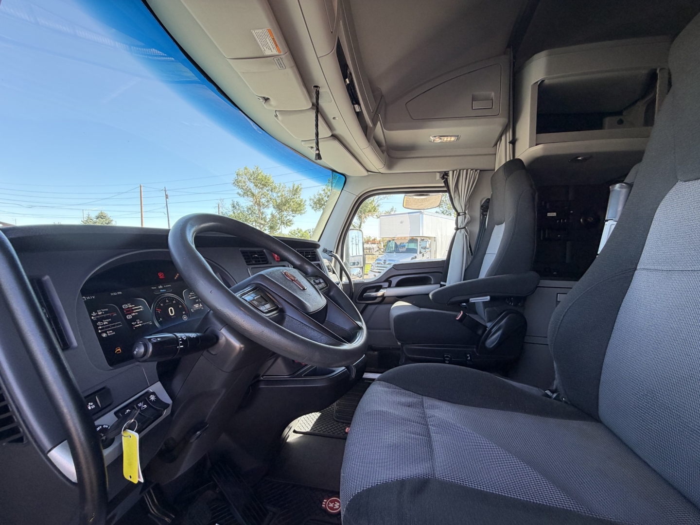 Kenworth truck interior cab view showing steering wheel, dashboard, and front seats; pilot seat and sleeper area visible.
