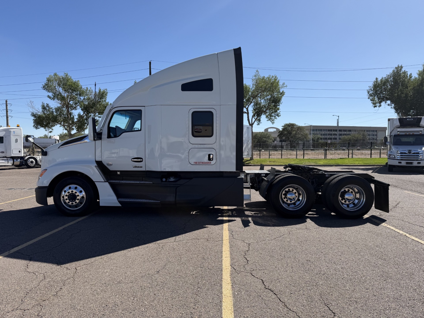 Kenworth T680 semi truck in a parking lot, side view showing sleeper cab, tandem rear axles, white exterior, no visible text readable.