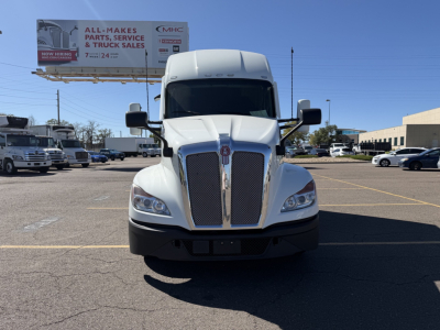 Kenworth T680 truck front view in a dealership lot with billboards and other vehicles in background.